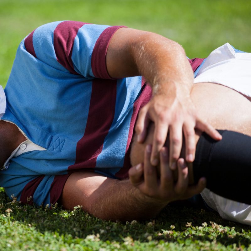 Injured rugby player holding their knee on the field
